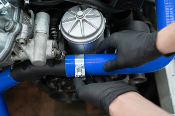 A car mechanic uses a metal clamp to secure a blue hose while performing maintenance in an auto...