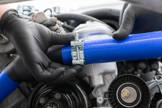A car mechanic uses a metal clamp to secure a blue hose while performing maintenance in an auto repair shop.