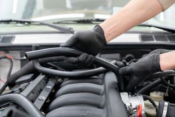 Mechanic works on installing air hose inside the engine compartment of a vehicle, ensuring proper function at an auto repair shop.