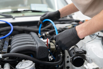 Fototapeta premium Hands in gloves attach a blue car vacuum hose to the engine while performing maintenance in a clean garage environment.