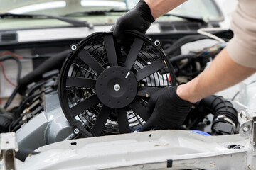 Technician handles an electronic fan while installing it in the engine compartment for proper...