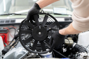 Technician handles an electronic fan while installing it in the engine compartment for proper cooling function in a car.