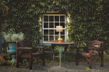 A charming outdoor patio in the Lake District, featuring a rustic bistro table and wooden chairs against an ivy-covered wall, exuding quaint village serenity.