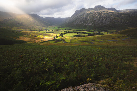 A breathtaking view of the Langdale Valley in the Lake District, showcasing dramatic Side Pike mountain and a serene rural landscape around the farmland of Cumbria, UK.