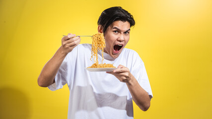 Asian man in white t-shirt excitedly holding a plate of noodles with one hand and lifting a portion...