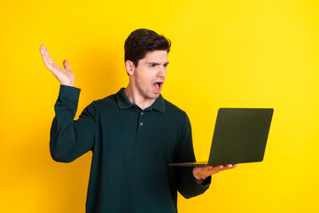 Surprised young man holding a laptop against a yellow background showcasing astonishment