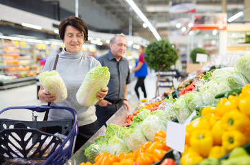 Mature female customer selects savoy cabbage with interest in grocery department of supermarket