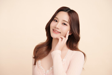 Fototapeta premium A beautiful young Asian woman with clean, fresh skin against a beige background. Skincare, facial treatment, cosmetology, beauty, and spa. An elegant portrait of an Asian woman.