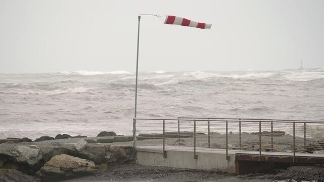 Red and White Wind Sleeve Blowing Above a Rocky Coastline