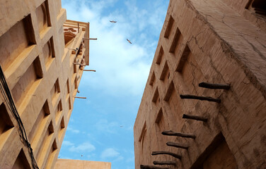 Stone walls of traditional architecture in the Old City district in Dubai and two seagulls flying against the blue sky