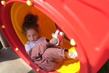Child in Playground Tunnel. Cute Girl Lying Inside a Colorful Playground Tunnel, close-up