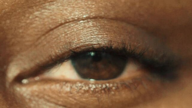 Gros plan artistique d&rsquo;un &oelig;il humain regardant la lumi&egrave;re, texture de peau visible, expression calme et myst&eacute;rieuse, portrait intime capturant les d&eacute;tails du regard et de la peau fonc&eacute;e