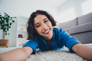 Young woman enjoying relaxing moments at home, smiling on a carpeted floor in a cozy and bright...