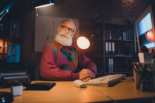Elderly man with beard working at computer in cozy office setting, showcasing professionalism and technology expertise