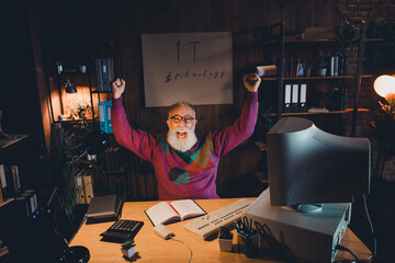 Excited mature man celebrating success at home office with computer in cozy room setting in the...