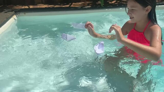 menina brinca com barcos de papel na piscina 