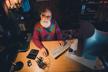 Elderly gentleman working at a desk in a cozy office setting with vintage computer equipment and...