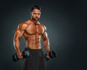 Muscular young man posing in studio holding dumbbells