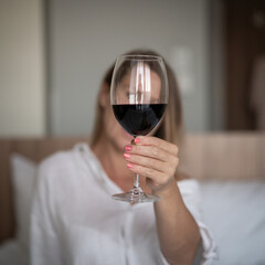 Young beautiful woman with a glass of wine sitting on the bed.