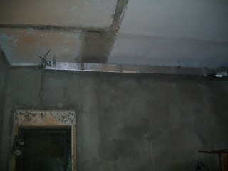 Construction work in a dimly lit space with exposed ceiling and duct work being installed