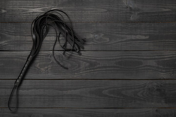 Black whip on wooden background, top view. BDSM concept