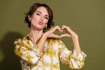 Confident young businesswoman making heart shape gesture in stylish khaki blouse against elegant background, conveying love and success in professional life