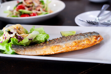 Grilled mackerel served on a white plate with fresh green salad, topped with creamy dressing and a slice of lime. A healthy and delicious seafood dish perfect for food content