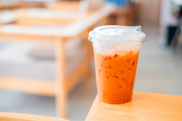 Ice Thai tea in clear plastic cup famous beverage drink traditional on wooden table in nature cafe, copy space