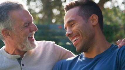 Senior Hispanic Man Talking And Laughing With Adult Son In Garden At Home