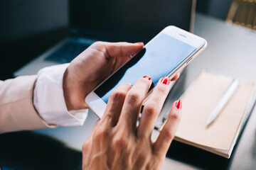 Fototapeta premium Cropped image of female millennial holding mobile phone for chatting and sending messages online , woman using modern smartphone connected to 4G for checking notification and mail in application