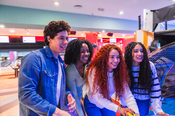 Four friends enjoying a friendly game of air hockey, laughing and having a great time together in a vibrant bowling alley
