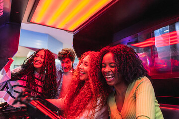 Four young friends laughing and playing an arcade game together in a bowling alley, enjoying their...