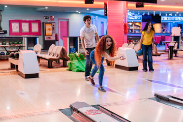 Group of friends enjoying a lively bowling game, laughing and throwing balls while sharing moments...