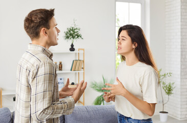 Unhappy young couple arguing at home, angry husband, wife blaming each other in life problems, conflicts in marriage, bad relationships, man and woman having quarrel, disagreement, misunderstanding