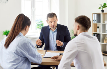 Young couple sitting at the desk and having consultation with mature man realtor or financial...