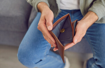 Close up of a man hands holding an empty, open wallet without cash, symbolizing financial...