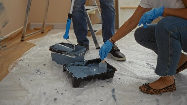 Couple painting home interior with blue paint together in new living room, showcasing indoor diy renovation scene with man and woman focused on creative teamwork.