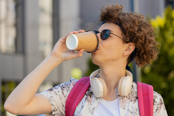 Happy Caucasian man tourist enjoying morning coffee hot drink and smiling. Relaxing, taking a break. Young guy walking on urban city center street, drinking coffee to go. Town lifestyles outside.