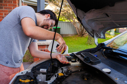 Young man working on car filling up engine coolant