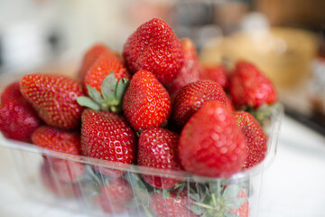 Plastic box full of ripe strawberries on kitchen table close up. Healthy eating.