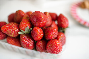 Plastic box full of ripe strawberries on kitchen table close up. Healthy eating.