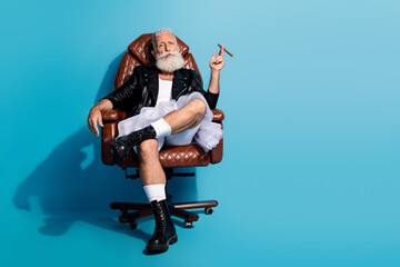 Obraz premium Photo of old man win dress skirt sit chair smoke cigar isolated on blue color background 