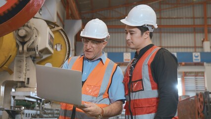 Engineer teaching apprentice to use metal sheet stamping machine, industrial team is working on various projects with laptop computer, worker work together to check the operation system in a factory