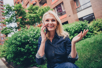 Smiling senior woman in denim enjoying a phone call in urban park setting on a sunny day