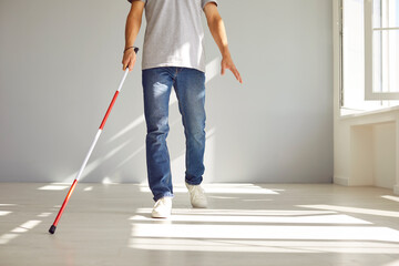 Cropped photo of legs of blind disabled man in casual clothes with long stick walking in empty room...