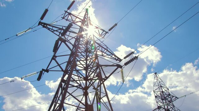 High-voltage supports with wires and insulators against the background of blue sky and flying clouds. Transmission of electricity by wires.
