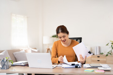 Fototapeta premium Woman holding document file stack of business document paper looking at laptop computer flicking through clients files on table, searching for and picking a file in home office.