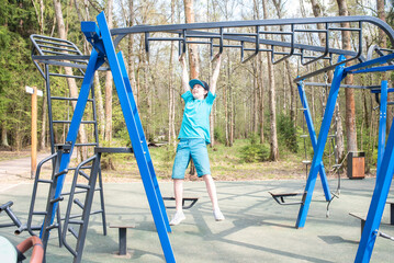 boy hanging by his hands and moving along a horizontal ladder (monkey walker) on a sports ground