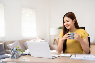 Asian business woman working on her project at home while drinking tea. Business woman relaxing while working in an office and drinking coffee during a break.
