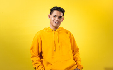 Asian man wearing a bright yellow hoodie smiling cheerfully while standing against vibrant yellow background, ideal for modern youth lifestyle, casual fashion, and creative branding visuals